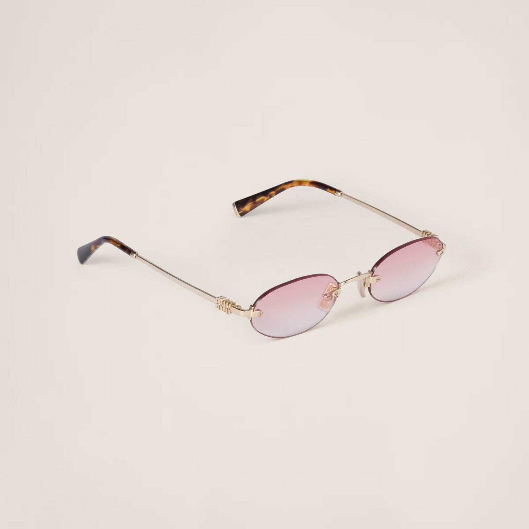 Image of Oval sunglasses with pinkish-red lenses, gold metal frame, and adjustable nose pads.