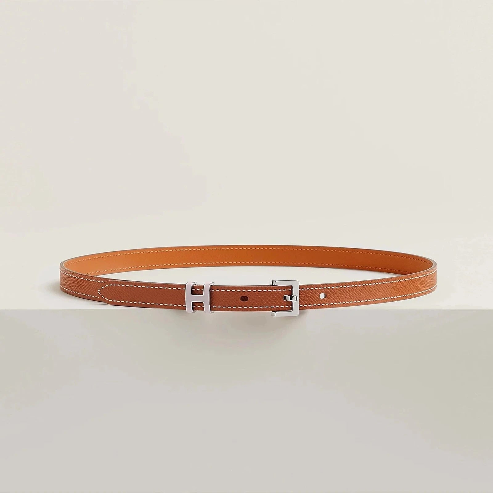 Luxurious Hermes leather belt with sleek metallic buckle on a minimalist design.