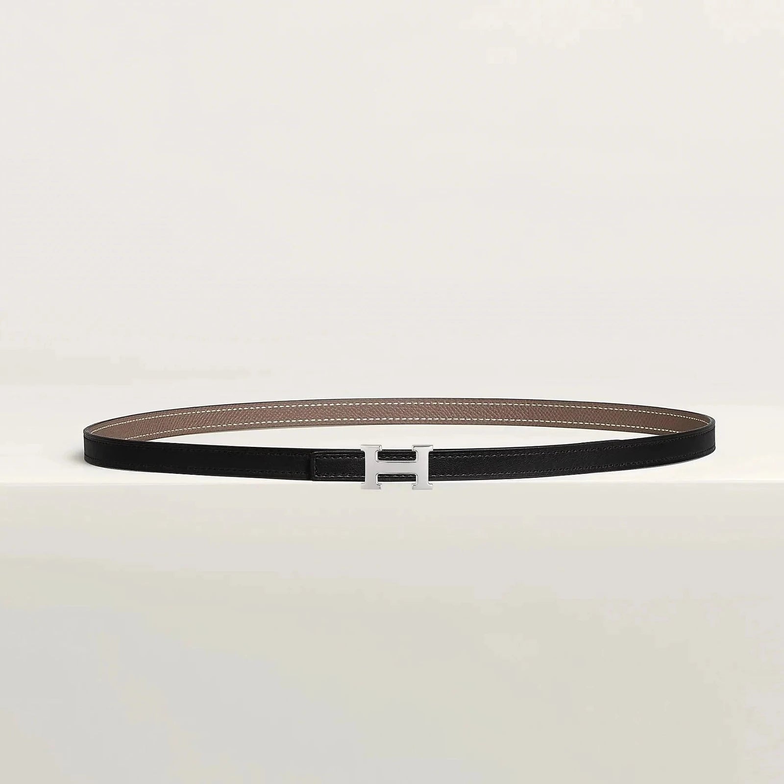 Hermes belt with metallic buckle on display, showcasing luxury craftsmanship and minimalist design.