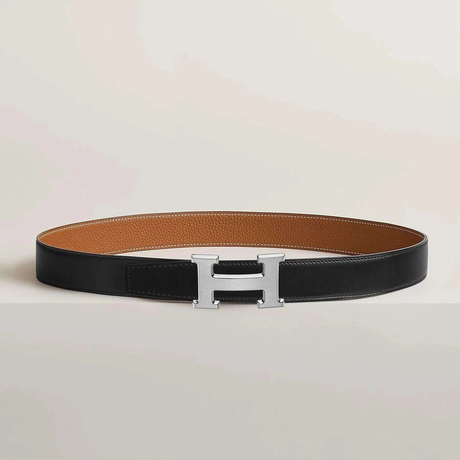 Image of Hermes belt with metallic H buckle, reversible leather design, elegant and minimalist.