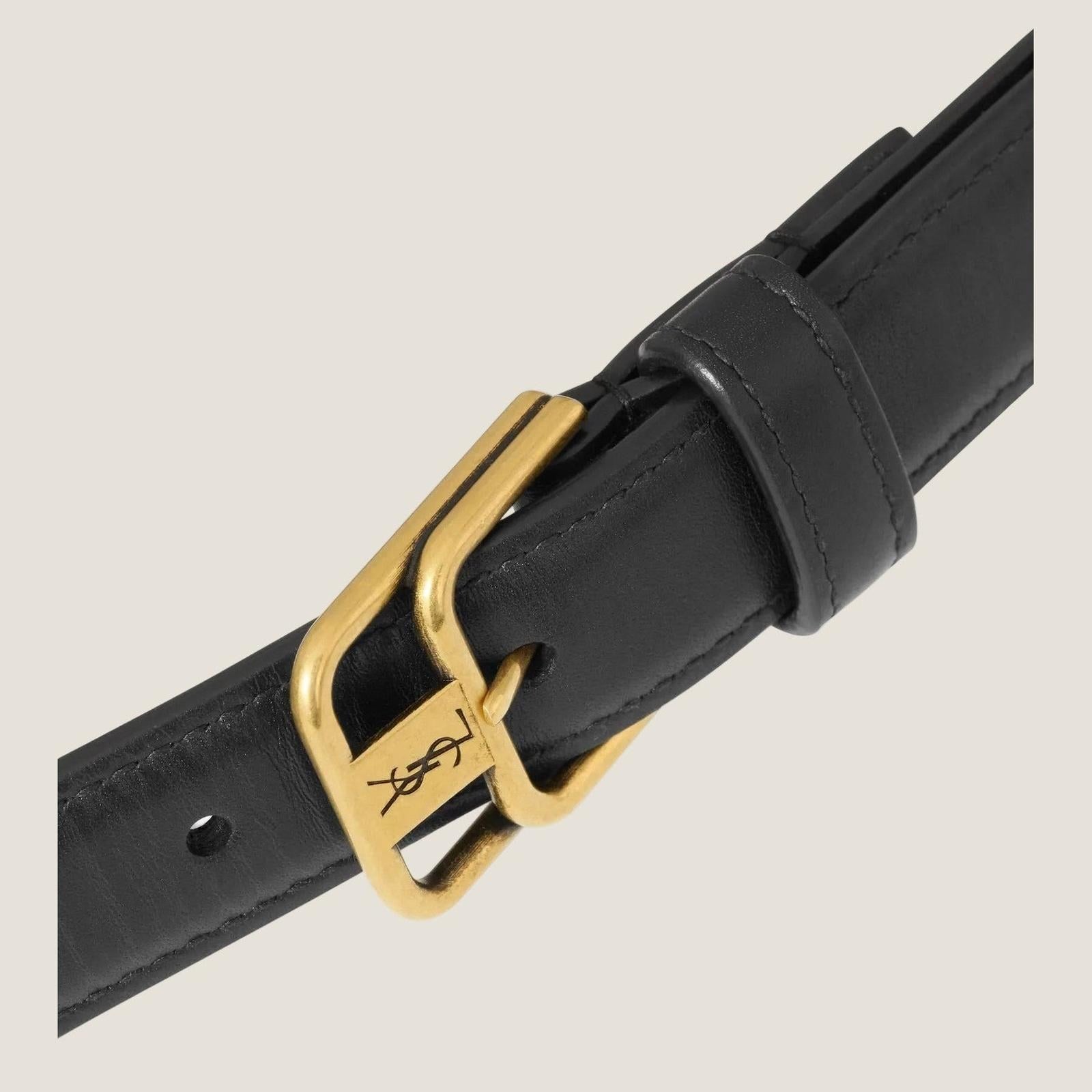 Image of תקריב האבזם הכפול הזהוב וחריטת YSL על הרצועה השחורה בחגורת CASSANDRE